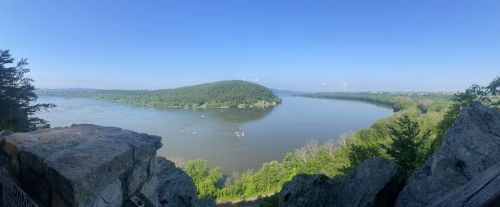 A panoramic view of a river winding around a green hill under a clear blue sky.