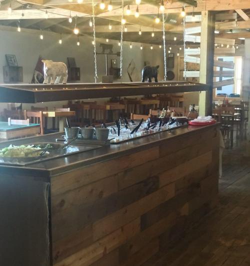 A rustic restaurant interior featuring a wooden buffet table with food options and string lights overhead.