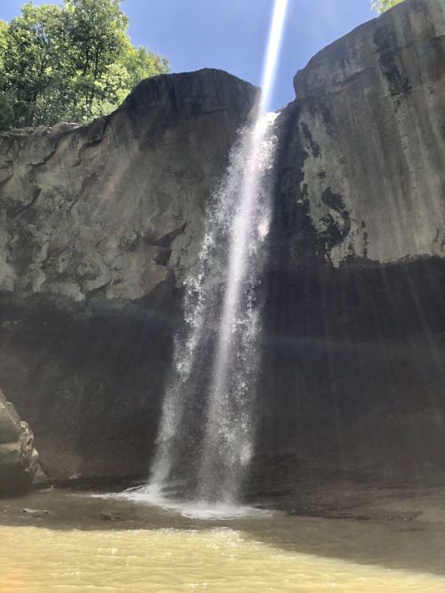 A waterfall cascades down rocky cliffs, with sunlight streaming through the mist, creating a serene natural scene.