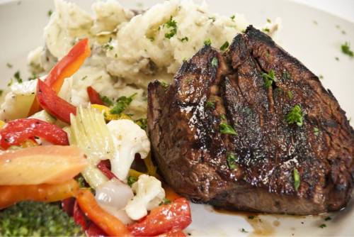 A plate featuring a grilled steak, creamy mashed potatoes, and a colorful medley of sautéed vegetables.