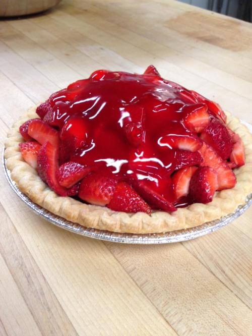 A freshly baked strawberry pie topped with glossy red glaze and sliced strawberries, sitting on a wooden surface.