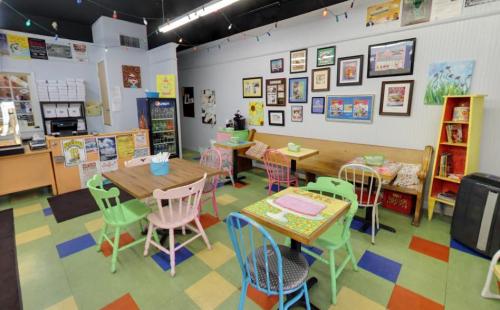 Colorful café interior with wooden tables, mismatched chairs, and framed artwork on the walls. Cozy and inviting atmosphere.