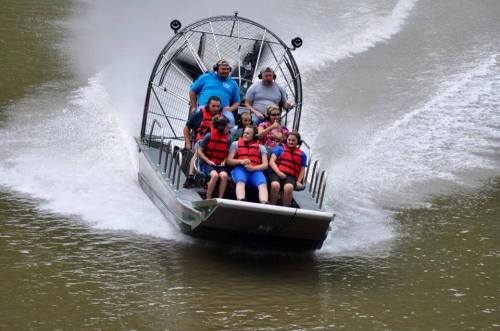 A group of people in life jackets enjoying a thrilling airboat ride on a river, splashing through the water.