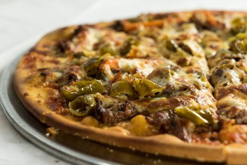 A close-up of a pizza topped with cheese, green peppers, and sausage on a silver pizza tray.