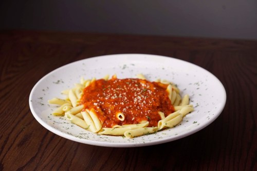 A plate of penne pasta topped with marinara sauce and sprinkled with cheese, garnished with herbs on a wooden table.