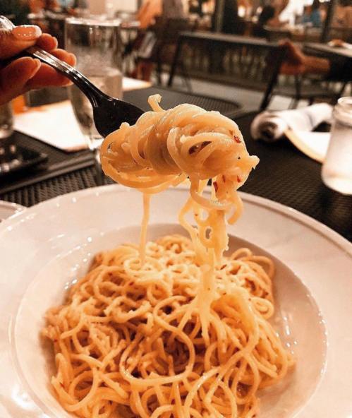 A fork lifts a serving of spaghetti from a bowl, with a blurred restaurant background.