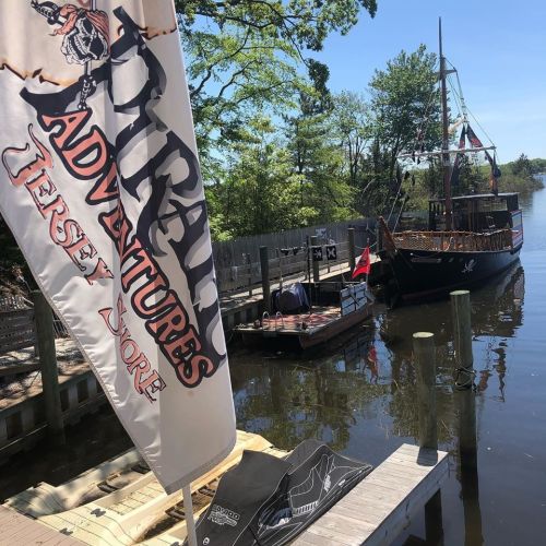A pirate-themed boat docked by a wooden pier, with a flag reading "Pirate Adventures Jersey Shore" in the foreground.