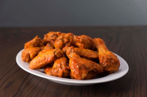 A plate of spicy chicken wings arranged neatly on a wooden table.