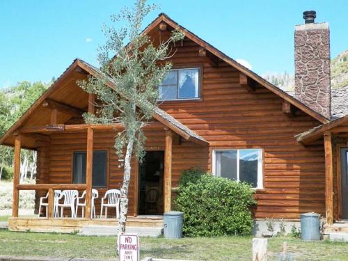 A rustic wooden cabin with a porch, chairs, and a stone chimney, surrounded by greenery and a "No Parking" sign.