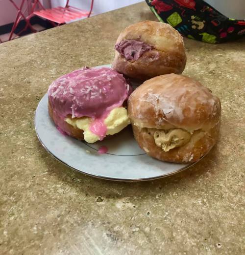 A plate with three filled donuts: one with pink icing, one with a creamy filling, and one glazed.