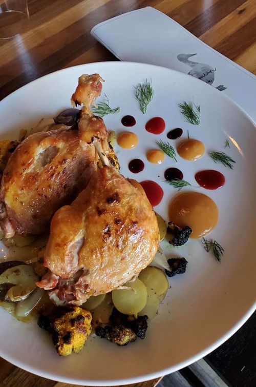 A plate featuring two roasted chicken legs on a bed of vegetables, garnished with colorful sauces and herbs.