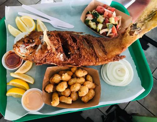 A platter featuring a whole fried fish, lemon wedges, onion, fried bites, and a side of fresh salad.