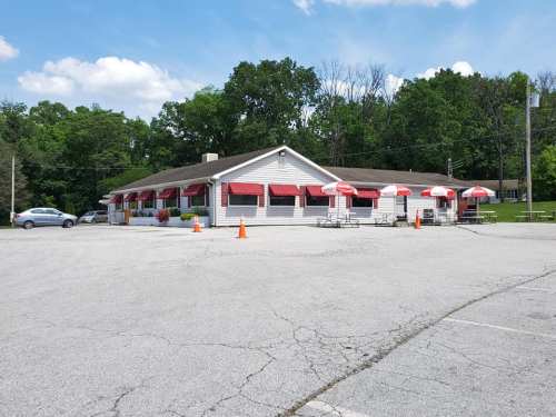 A single-story restaurant with red awnings and outdoor seating, surrounded by trees and a parking lot.