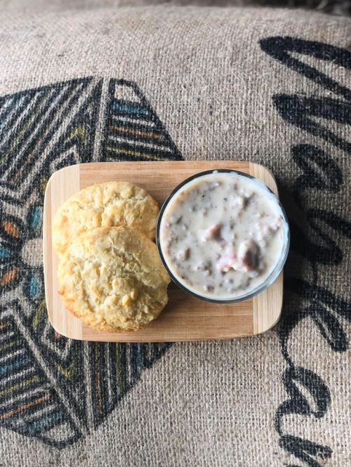 A wooden board with two biscuits and a bowl of creamy soup on a textured fabric background.