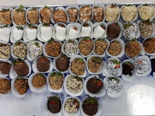 A variety of decorated chocolate-covered strawberries arranged in paper cups, featuring different toppings and flavors.
