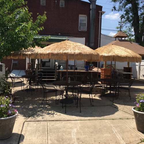 Outdoor seating area with thatched umbrellas, black metal tables, and chairs surrounded by potted flowers.