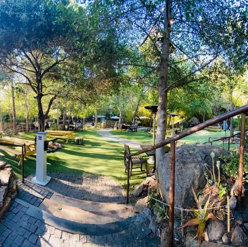 A serene park scene with green grass, trees, benches, and a pathway leading into a shaded area.