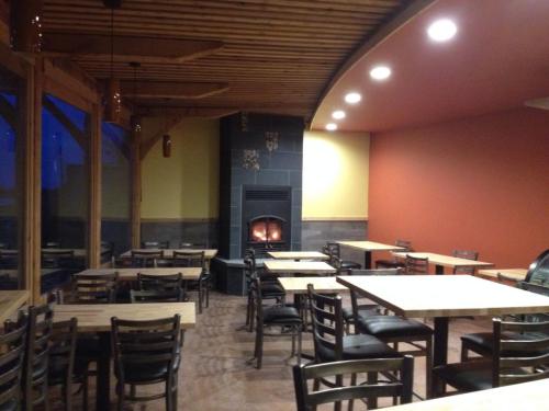 Cozy restaurant interior with wooden tables, chairs, and a fireplace, featuring warm colors and large windows.