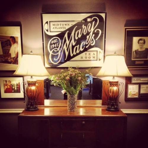 A cozy room featuring a sign for Mary Mac's Tea Room, with lamps, flowers, and framed photos on the walls.