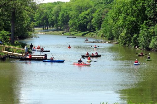 A serene river scene with people kayaking and canoeing among lush green trees on a sunny day.