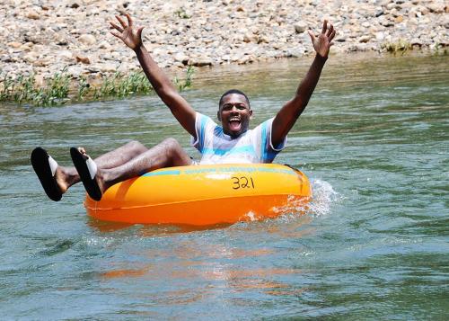 A person joyfully floating on an orange inner tube in a river, with arms raised and a big smile.