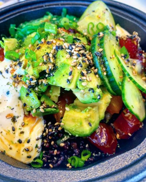 A colorful bowl featuring black rice, avocado, cucumber, cherry tomatoes, green onions, and sesame seeds.