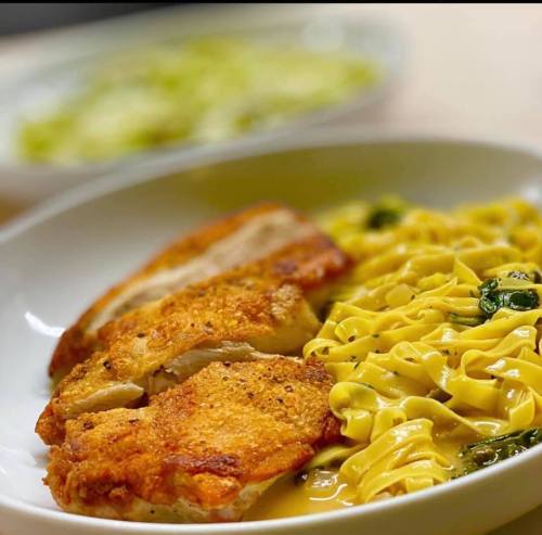 A plate of crispy chicken served with creamy fettuccine pasta and greens in the background.