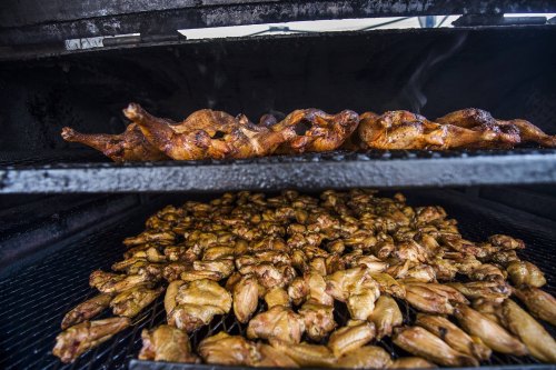 A barbecue smoker filled with grilled chicken wings and whole chickens, showcasing a smoky cooking environment.