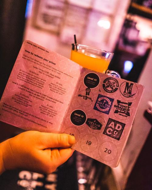 A hand holds a drink menu with stamps and instructions for redeeming prizes at a bar.