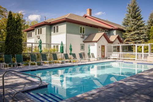A serene outdoor pool area with lounge chairs, surrounded by greenery and a charming building in the background.
