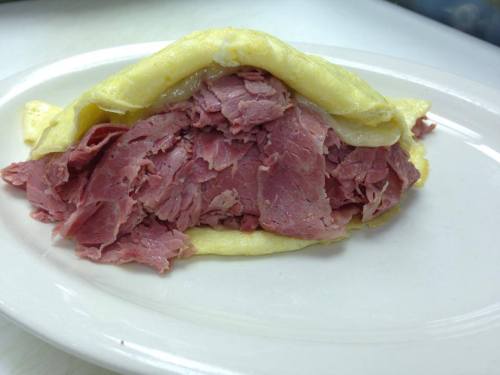 A plate featuring a large omelet filled with shredded pink corned beef.