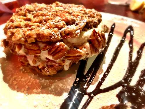 A delicious dessert featuring a cookie sandwich filled with cream and topped with nuts, drizzled with chocolate sauce.