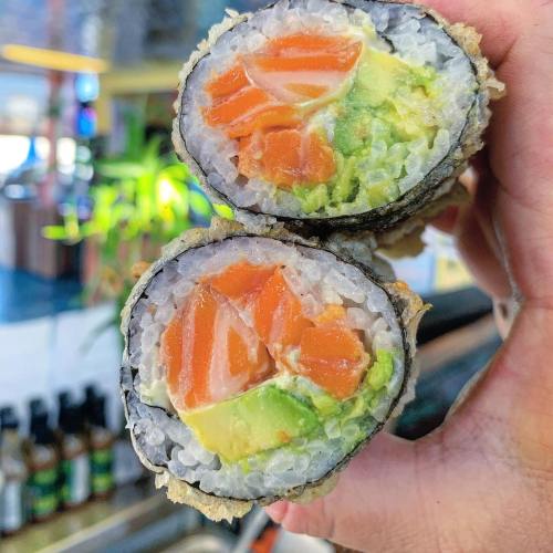 Close-up of a hand holding a cut sushi roll, revealing layers of salmon, avocado, and rice wrapped in seaweed.