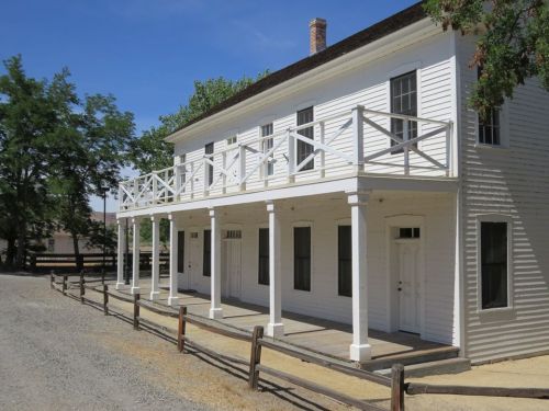 Historic white building with a balcony, surrounded by trees and gravel, showcasing a classic architectural style.