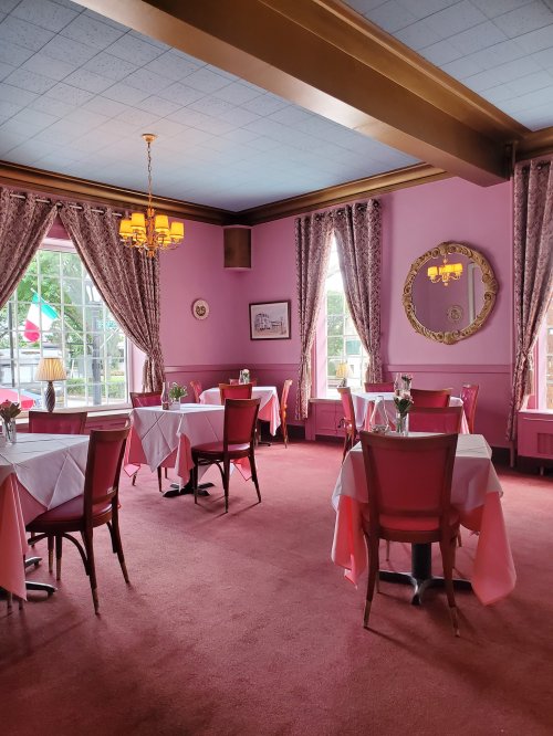 A cozy restaurant interior with pink walls, tables set with white tablecloths, and elegant decor.