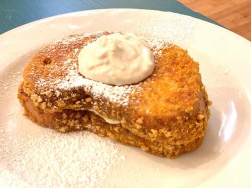 A slice of French toast topped with whipped cream and dusted with powdered sugar on a white plate.