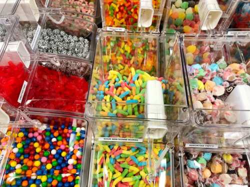 A colorful assortment of candies in clear bins, including gummy worms, taffy, and various gummies.