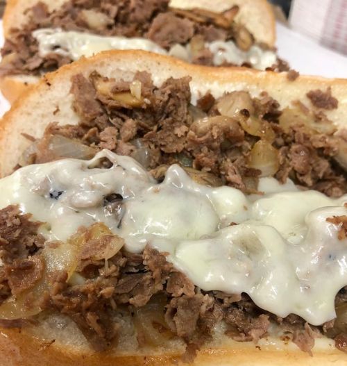Close-up of a sandwich filled with shredded beef, sautéed onions, and melted cheese on soft bread.