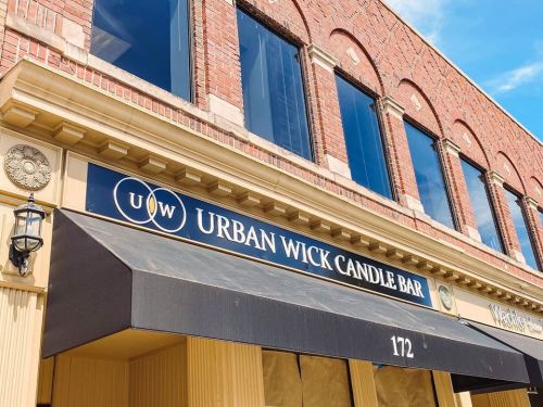 Sign for Urban Wick Candle Bar on a brick building, featuring large windows and an awning. Address: 172.