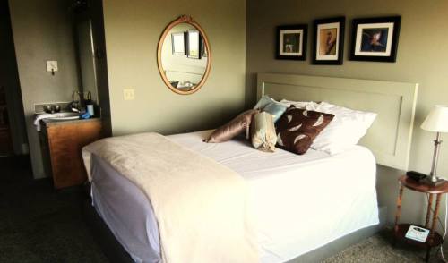 Cozy bedroom featuring a bed with decorative pillows, a mirror, framed photos, and a small bedside table.
