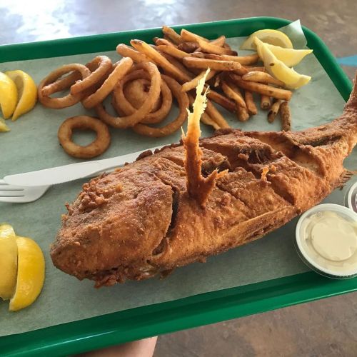 A tray with a whole fried fish, onion rings, French fries, and lemon wedges, accompanied by dipping sauces.