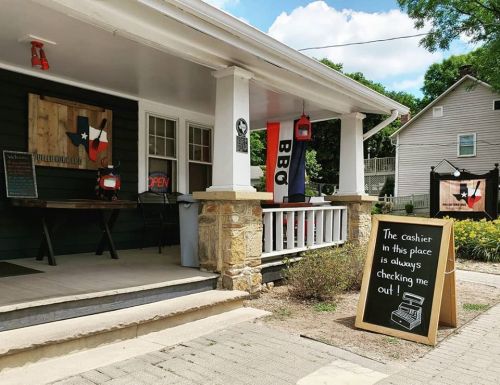 A charming BBQ restaurant with a welcoming porch, featuring a sign that reads, "The cashier in this place is always checking me out!"