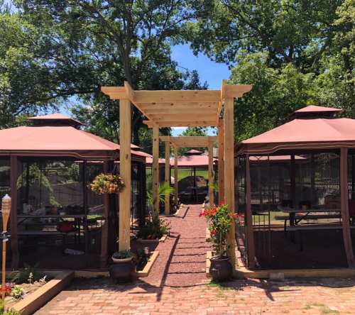 A pathway lined with wooden structures leads to several gazebo-style seating areas surrounded by greenery.