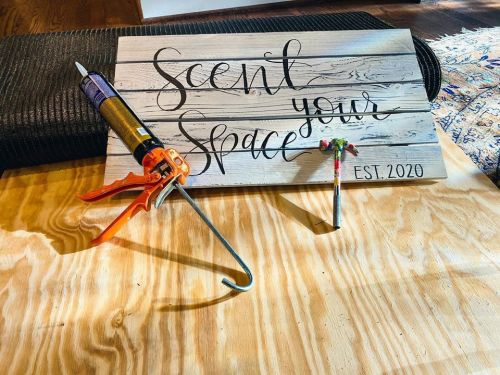 A wooden sign reading "Scent your space" with tools and a paintbrush on a wooden surface.