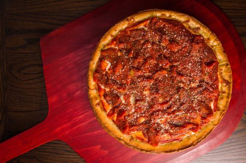 A freshly baked pizza with a thick crust, topped with marinara sauce and sprinkled with herbs, on a wooden pizza peel.