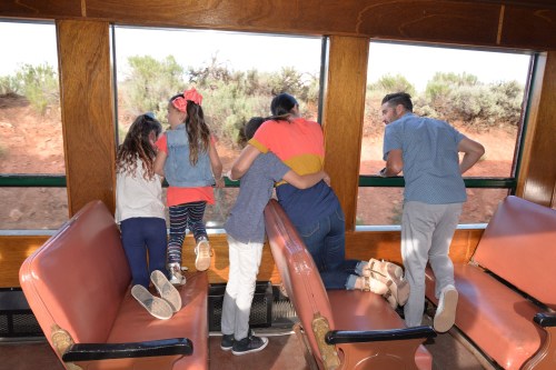 A group of children and adults lean out of a train window, looking at the scenery outside.