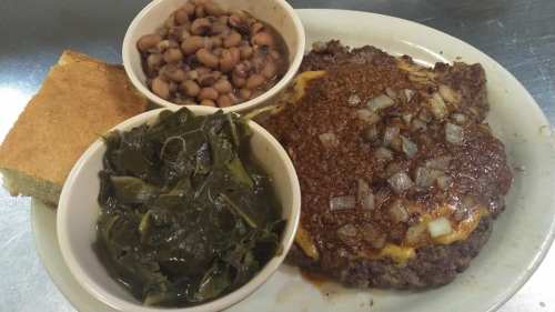 A plate featuring a beef patty topped with onions, cornbread, black-eyed peas, and collard greens.