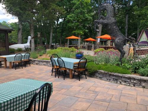 Outdoor dining area with checkered tables, surrounded by greenery and a large horse sculpture in a park-like setting.