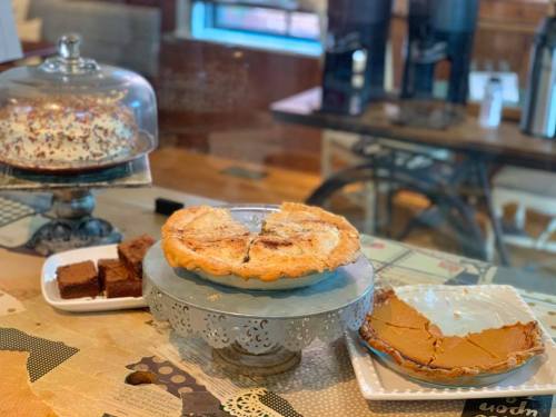 A display of desserts including a pie, pumpkin bars, and brownies on decorative stands in a cozy setting.