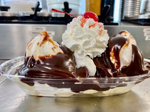 A delicious ice cream sundae with two scoops, chocolate sauce, whipped cream, and a cherry on top in a glass dish.